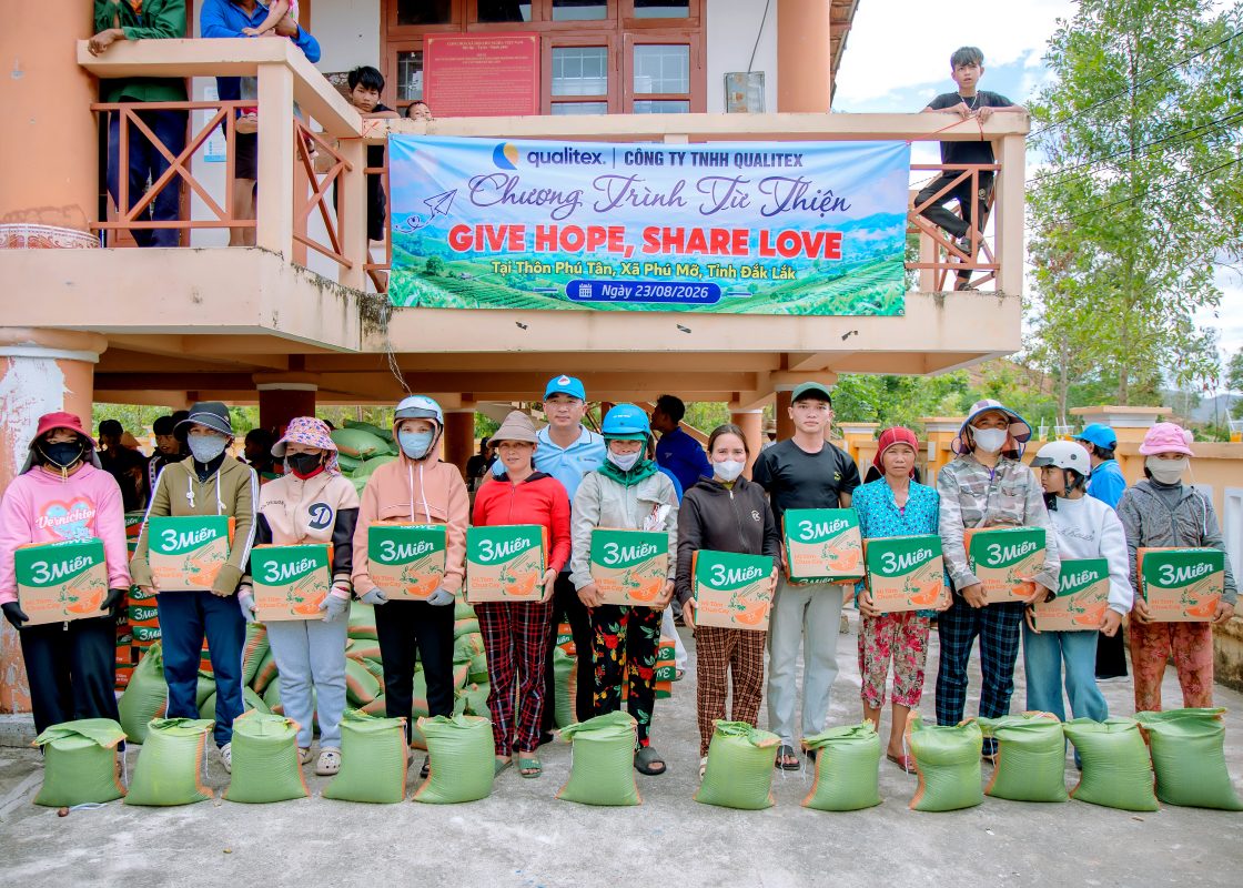 Villagers in Phu Tan holding gift cartons from the Qualitex charity program in front of the Give Hope, Share Love banner